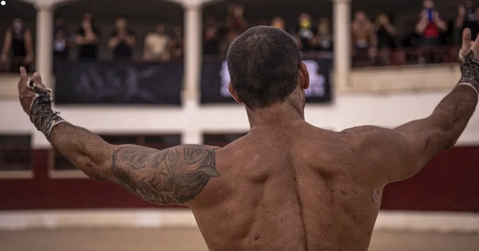 Tattooed performer facing an audience with arms outstretched