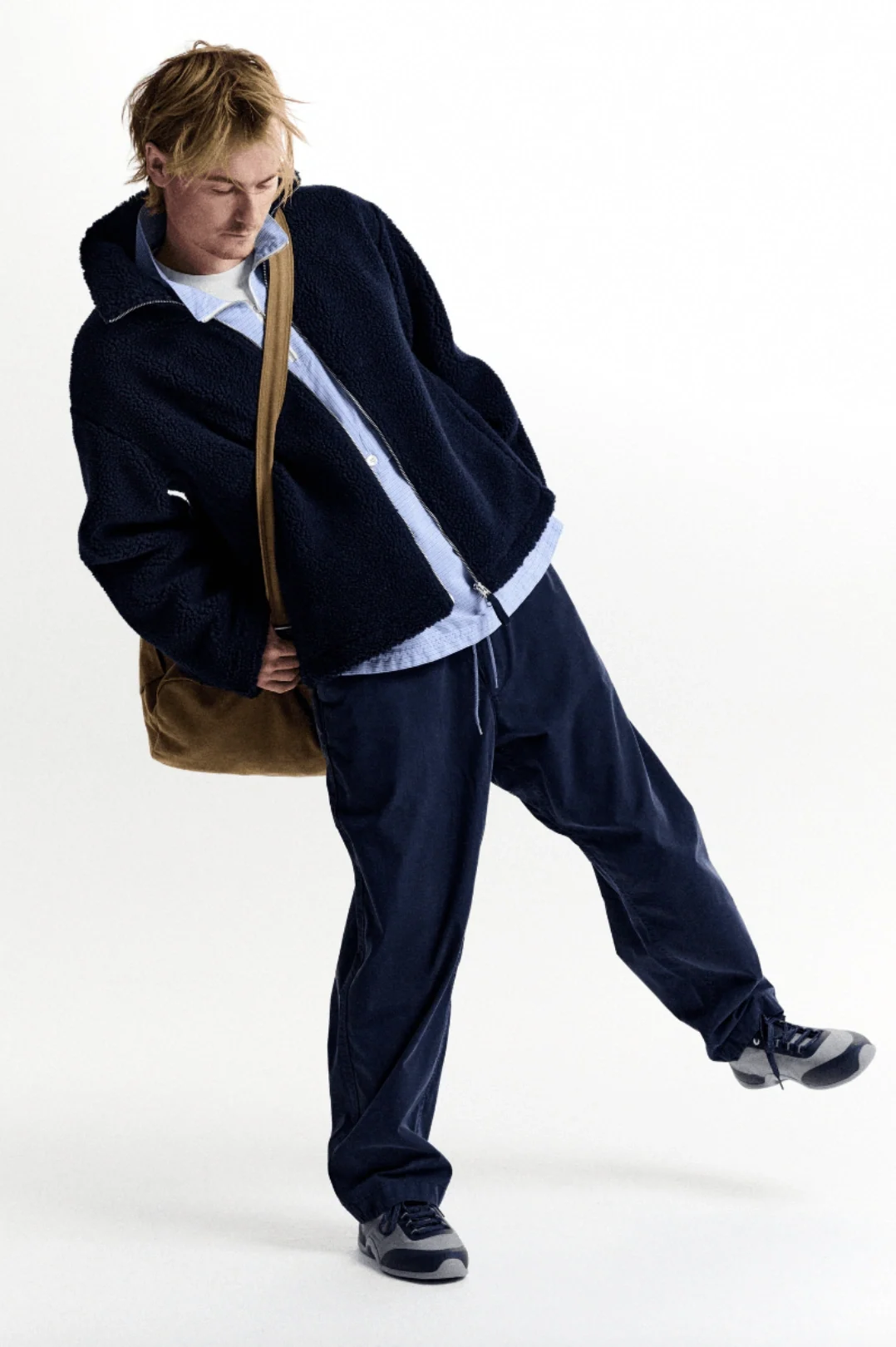 Model in navy clothing and a shoulder bag against a white backdrop