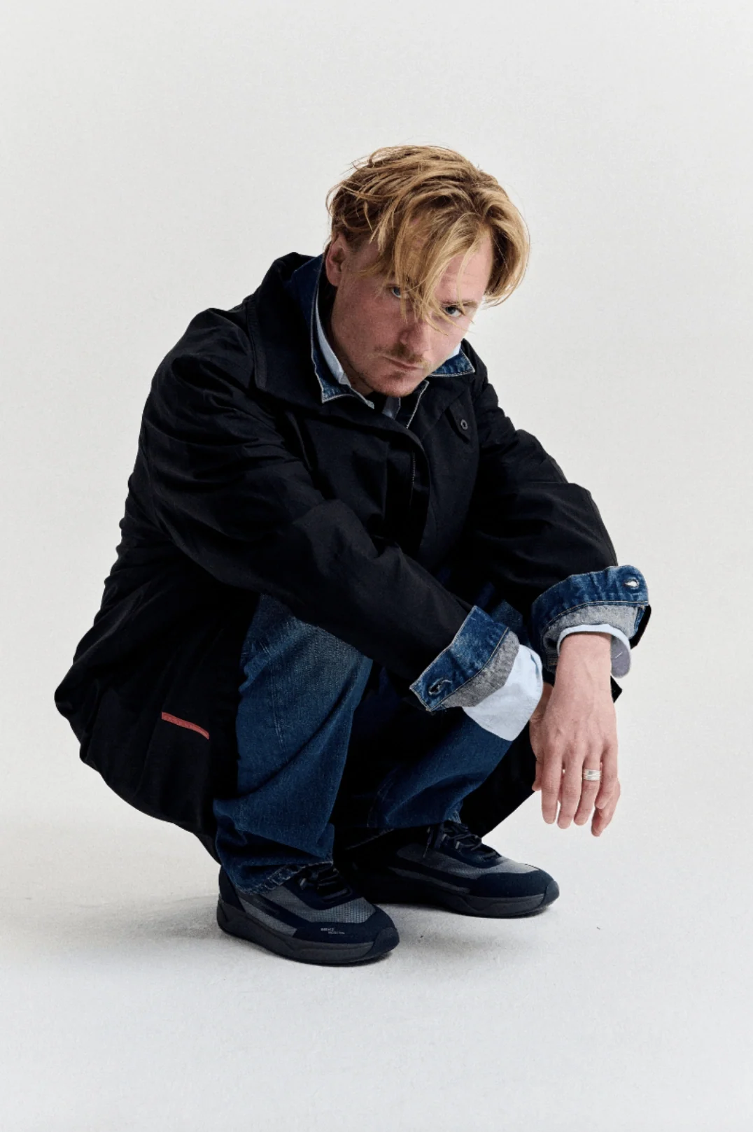 Crouching model wearing a navy coat and jeans