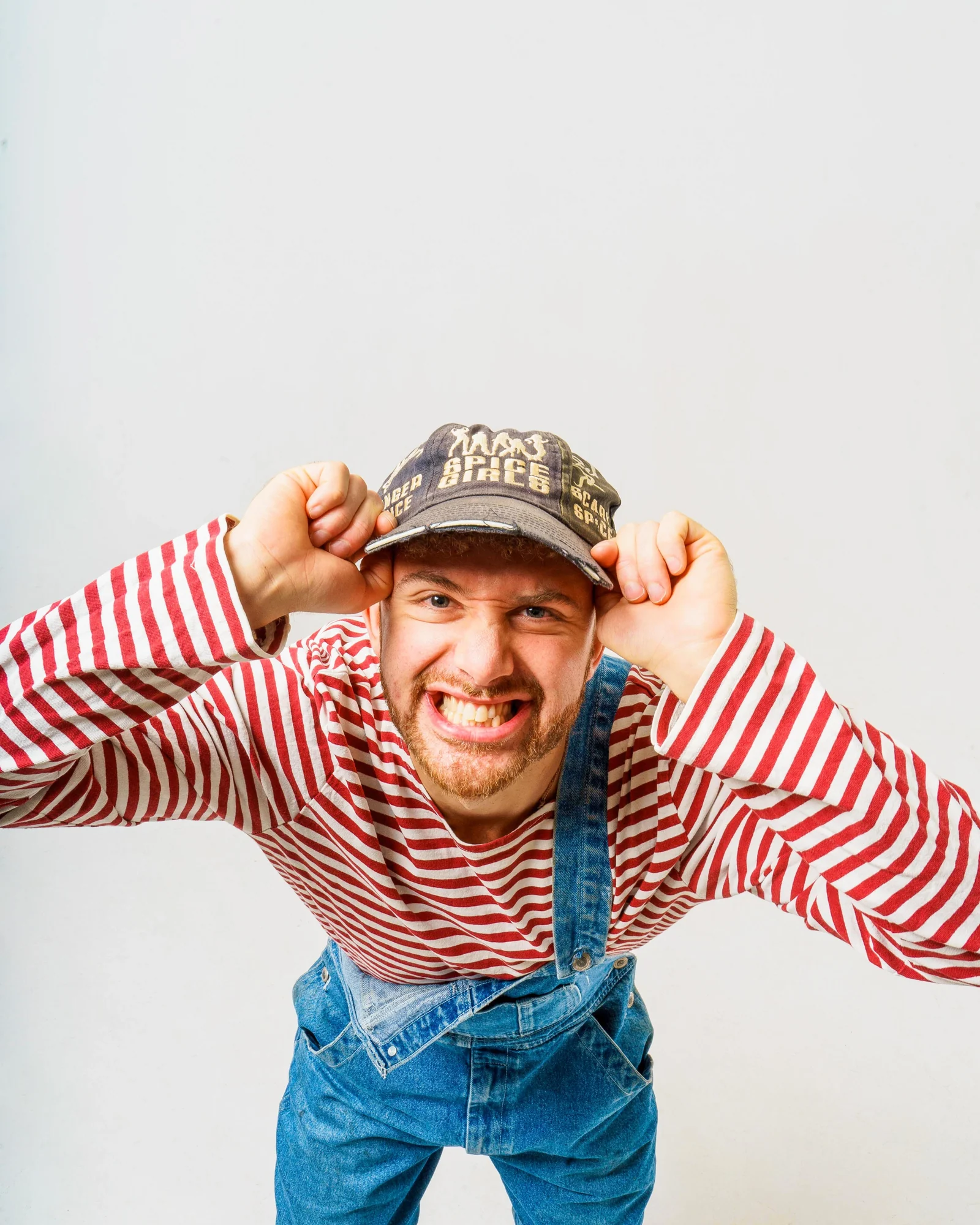 Smiling musician in a red-and-white striped top and denim overalls holding his cap.